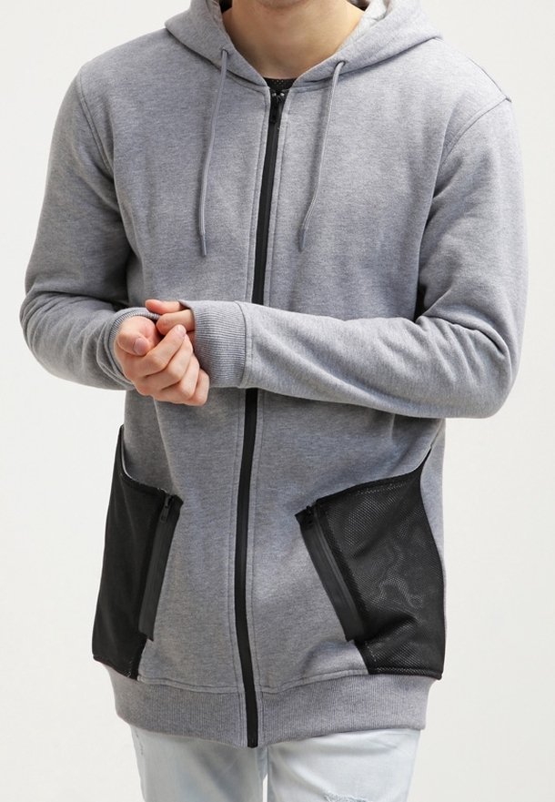 Felpa grigia con zip in tessuto misto cotone, con tasche in mesh nero, cappuccio con coulisse e polsini a coste. Vestibilità comoda, lunghezza media.