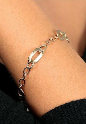Gold chain bracelet features oval and circular links, with a smooth finish. The bracelet is worn on a wrist, contrasting with skin tone.