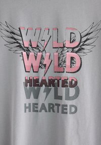 Grå t-shirt med teksten "WILD HEARTED" i forskellige størrelser og farver: pink, mørkegrå og sort, med grafik af vinger og lyn.