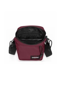 Borsa Eastpak color marrone con zip sulla parte superiore, interno nero, tracolla regolabile e patch con logo. Tessuto liscio con una forma rettangolare semplice.
