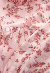 Tissu rose avec petits motifs floraux mauves et verts et accents carrés métalliques argentés, avec des parties froncées et à volants.