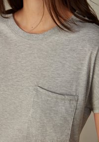 Camiseta gris de manga corta hecha de una tela suave, con un bolsillo en el pecho y un cuello redondo con detalles de costura.