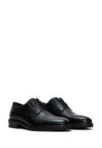 Zapatos de cuero negro con cordones, acabados texturizados, punta redondeada y suela de goma resistente. Presentan un diseño suave con costuras mínimas.