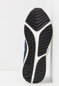 Tmavě modrá podešev tenisky s černým gumovým vzorkem, bílá mezipodešev a texturované detaily. Velikost 37. Název značky "WODEN" vyražený na boku.