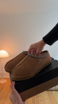 Tan suede instappers met een gepatterneerde, contrasterende rand, ronde neusvorm en een gestructureerde rubberen zool. Merklogo zichtbaar aan de zijkant.