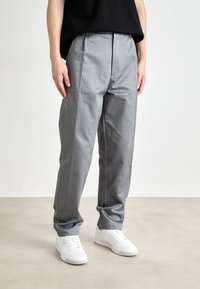 Grå formella byxor med en mjuk textur och en avslappnad passform, med framfåll och sidofickor, kombinerade med vita sneakers.