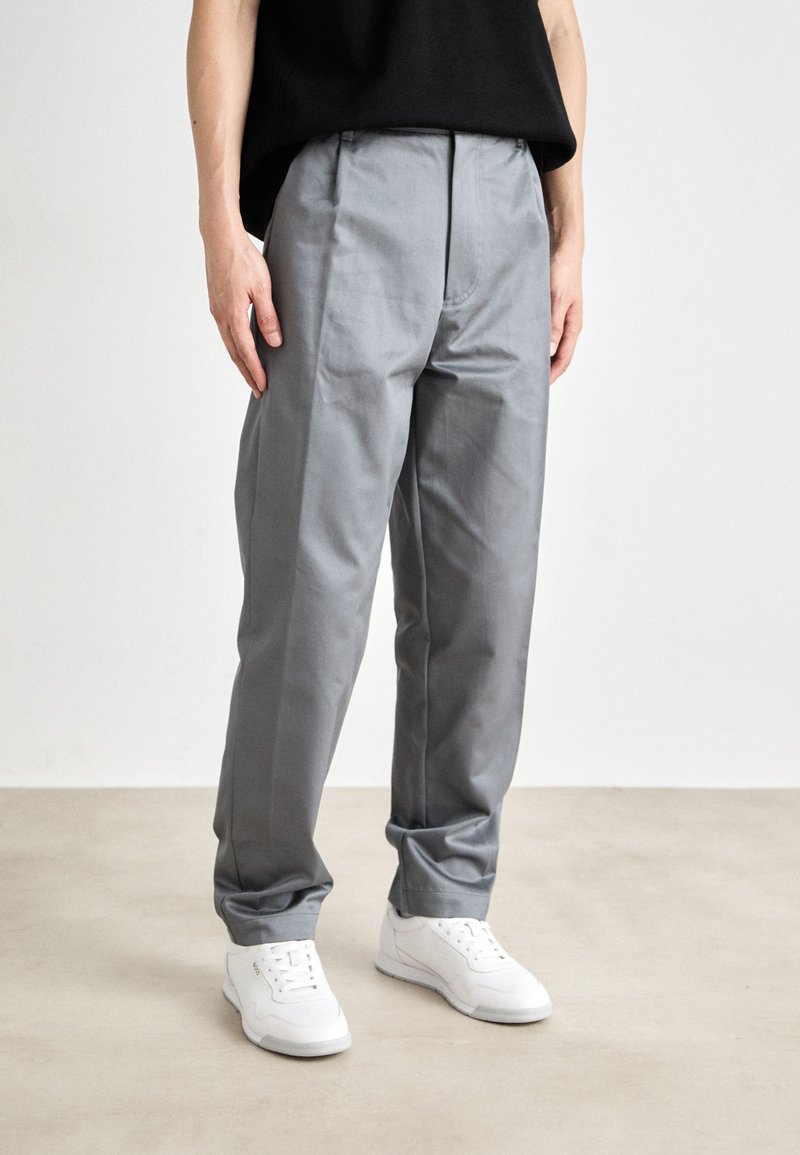 Grå formella byxor med en mjuk textur och en avslappnad passform, med framfåll och sidofickor, kombinerade med vita sneakers.