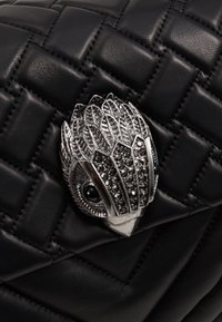 Černá prošívaná kožená kabelka s stříbrnou broží ve tvaru sovy, zdobená třpytivými černými kameny a propracovanými detaily peří.