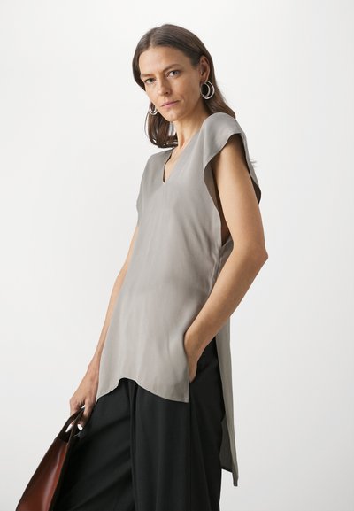 Light grey, sleeveless blouse with a V-neck and side slits. Soft fabric with a smooth texture; paired with black wide-leg trousers and a brown bag.