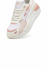 Baskets blanches et rose clair Puma avec lacets, panneaux en mesh et cuir, et semelle épaisse rembourrée, présentées en angle pour montrer le côté et l’avant.