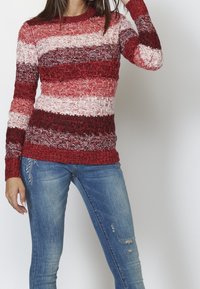 Czerwono-biała sweter z prążkowanym wzorem, okrągłym dekoltem i długimi rękawami, zestawiony z zniszczonymi dżinsami.