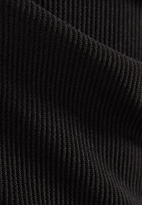 Svart ribbat tyg med en texturerad yta. Materialet har upphöjda åsar som skapar ett mönster, vilket betonar djup och struktur.