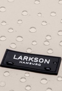 Tessuto color crema con gocce in rilievo, con un'etichetta nera che recita "LARKSON HAMBURG" in basso, che mostra una superficie testurizzata.