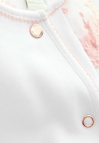Biała odzież z różowymi przeszyciami, z okrągłym akcentem w kolorze różowego złota i detalem guzika. Miękka tkanina z delikatnym kwiatowym wzorem.