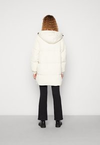 Dikke witte parka met een capuchon, met een gequilt ontwerp en elastische mouwen, gecombineerd met zwarte flared broek en chunky zwarte laarzen.
