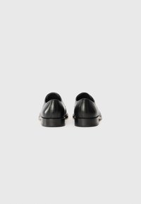 Black leather shoes with a smooth finish, rounded toe, low heel, and stitched detailing on the heel and sides. Sole is textured.