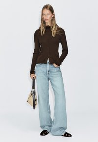 Dark brown ribbed cardigan with button closures, paired with light blue wide-leg jeans. Carrying a patterned bag and wearing black sandals.