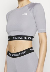 Persona que lleva una camiseta corta de manga corta color púrpura claro de North Face y leggings a juego con bandas elásticas negras con la marca "THE NORTH FACE".