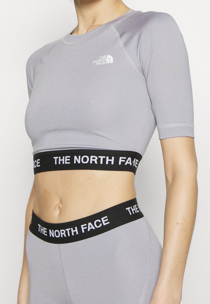 Persona que lleva una camiseta corta de manga corta color púrpura claro de North Face y leggings a juego con bandas elásticas negras con la marca "THE NORTH FACE".