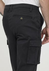 Pantalons cargo noirs avec une texture lisse, dotés de plusieurs poches, d'une touche de bouton et d'une taille ajustée.