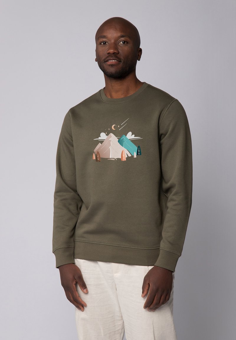 Un sweat-shirt vert olive avec un graphisme représentant une scène de montagne dans des couleurs pastel, col rond, manches longues, et poignets et ourlet côtelés.