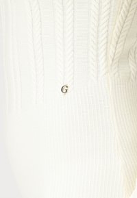 Maglione bianco lavorato a maglia con motivo a treccia, texture a coste e un piccolo logo dorato "G" accentato nella parte inferiore.