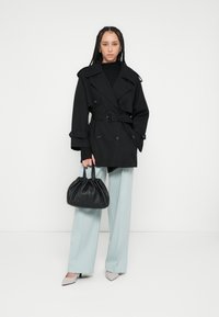 Czarny dwurzędowy płaszcz trencz z paskiem, zestawiony z jasnoniebieskimi spodniami o szerokich nogawkach i czarną, marszczoną torebką. Buty z ostrym noskiem.