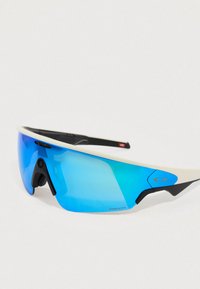 Gafas de sol con montura blanca y lentes con tintado azul. Presentan un diseño aerodinámico y un logo prominente, con detalles texturizados en las patillas.