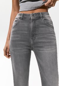 Jean en denim gris avec une taille haute, comportant des poches avant, une fermeture à bouton et une texture de tissu lisse. Design minimaliste.