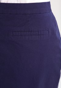 Námořnická modrá sukně s hladkým povrchem, vybavená malou kapsičkou na zadní straně a jednoduchým designem pasu.