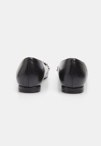 Black leather ballet flats with a small heel, featuring gold-tone hardware accents and a smooth, glossy texture. Rounded toe design.