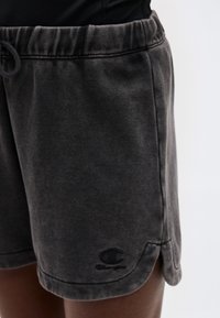 Κοντινό πλάνο ενός ατόμου που φοράει σκούρα γκρι σορτς Champion με ελαστική μέση και λογότυπο κοντά στο τελείωμα.