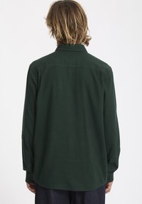 Chemise verte à manches longues en tissu doux, avec un col classique, des poignets boutonnés et une coupe droite. La vue arrière montre un design simple.