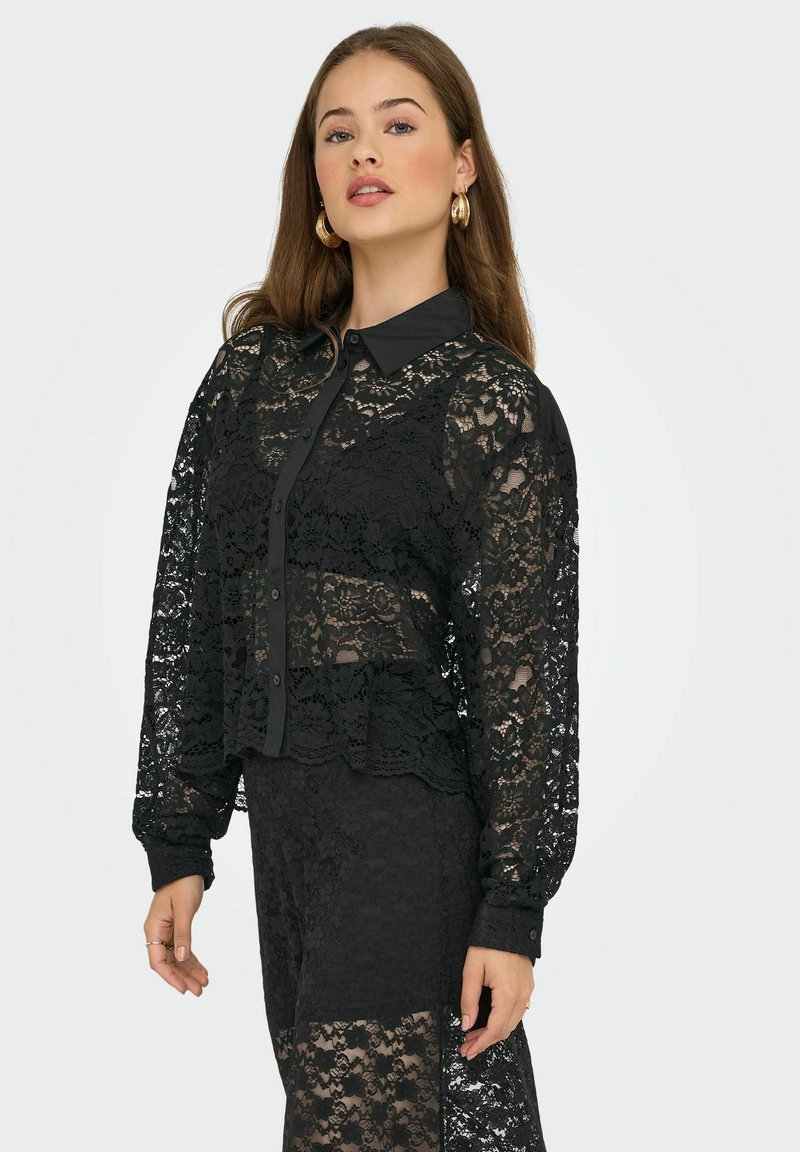 Blouse en dentelle noire avec un col, fermeture à boutons et manches longues. Présente des motifs floraux et un design court et superposé.