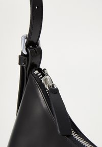 Borsa a spalla in pelle nera con forma triangolare, dettagli metallici argentati, chiusura con zip e una superficie liscia con tracolla corta.