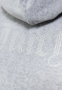 Felpa grigia con una texture morbida, caratterizzata da un logo "Juicy" scintillante e impreziosito da strass, scritto in un font curvo sul davanti.