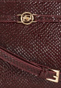 Burgundy textured leather bag with a glossy finish, featuring a gold circular logo and matching strap with a gold buckle detail.