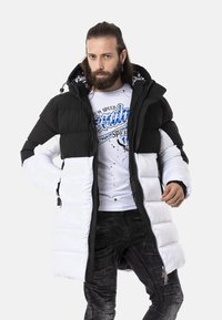 Schwarze und weiße Pufferjacke mit Reißverschluss, Kapuze und gestepptem Design. Der weiße untere Teil und die Ärmel stehen im Gegensatz zum soliden schwarzen oberen Teil.