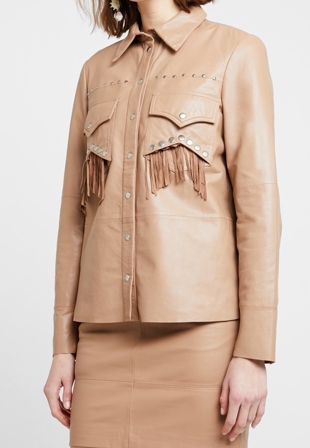 Läderjacka i brun färg med fransdetaljer på bröstfickorna, silvernitar längs axlarna, knäppning fram och långa ärmar. Slät textur.