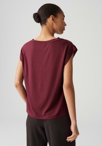 Top corto bordeaux a maniche corte con una vestibilità rilassata, scollatura ampia e tessuto morbido. Texture liscia con cuciture minime e senza pattern notevoli.