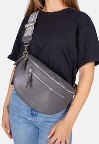 Sac de crossbody en cuir gris avec une texture en relief, deux poches zippées et une bandoulière ajustable à motifs. Forme ronde et accents en quincaillerie argentée.