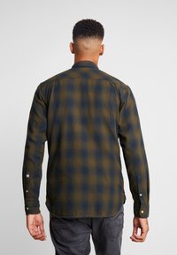 Camicia a maniche lunghe in tela scozzese verde scuro e blu navy, con colletto abbottonato, polsini e una vestibilità comoda. Presenta un tessuto testurizzato.