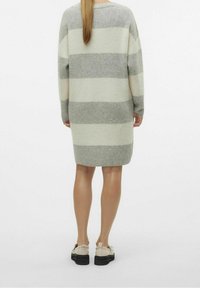 Robe tricotée rayée gris et blanc, coupe ample, col arrondi et manches longues, associée à des chaussures claires avec une semelle noire épaisse.