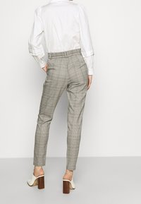 Grå rutig byxor i ett mjukt tyg, med ett elastiskt midjeband för komfort. Outfiten inkluderar en vit långärmad skjorta och beige klackar.