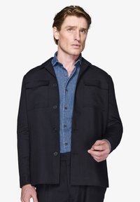 Sort jakke, letvægtsstof, lige snit, to forlommer, parret med en blå denimskjorte med knaplukning og krave.