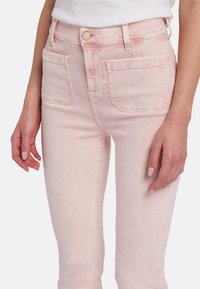 Jean en denim rose clair avec une texture lisse, taille haute et deux poches arrière. Doté d'une fermeture par bouton et zip à l'avant.