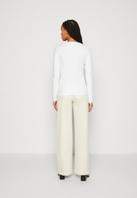 Langermet hvit topp kombineres med lysebeige vide bukser. Glatt tekstur, avslappet passform og et enkelt design uten synlige mønstre.
