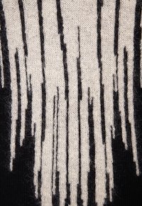 Tessuto a maglia nero con un motivo a righe verticali color crema, caratterizzato da una texture irregolare tipo frange che crea un aspetto stratificato.