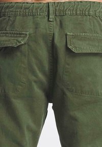 Zielono-oliwkowe spodnie cargo wykonane z miękkiej bawełny, z elastycznym paskiem ze sznurkiem i dwiema dużymi kieszeniami na plecach.