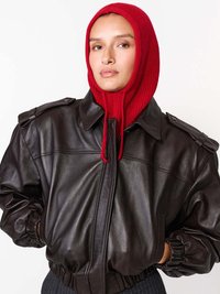 Hnědá kožená bomber bunda s žebrovanými manžetami, vyznačující se vysokým límcem a zapínacími ramenními epauletami, doplněná červenou pletenou kapucí.